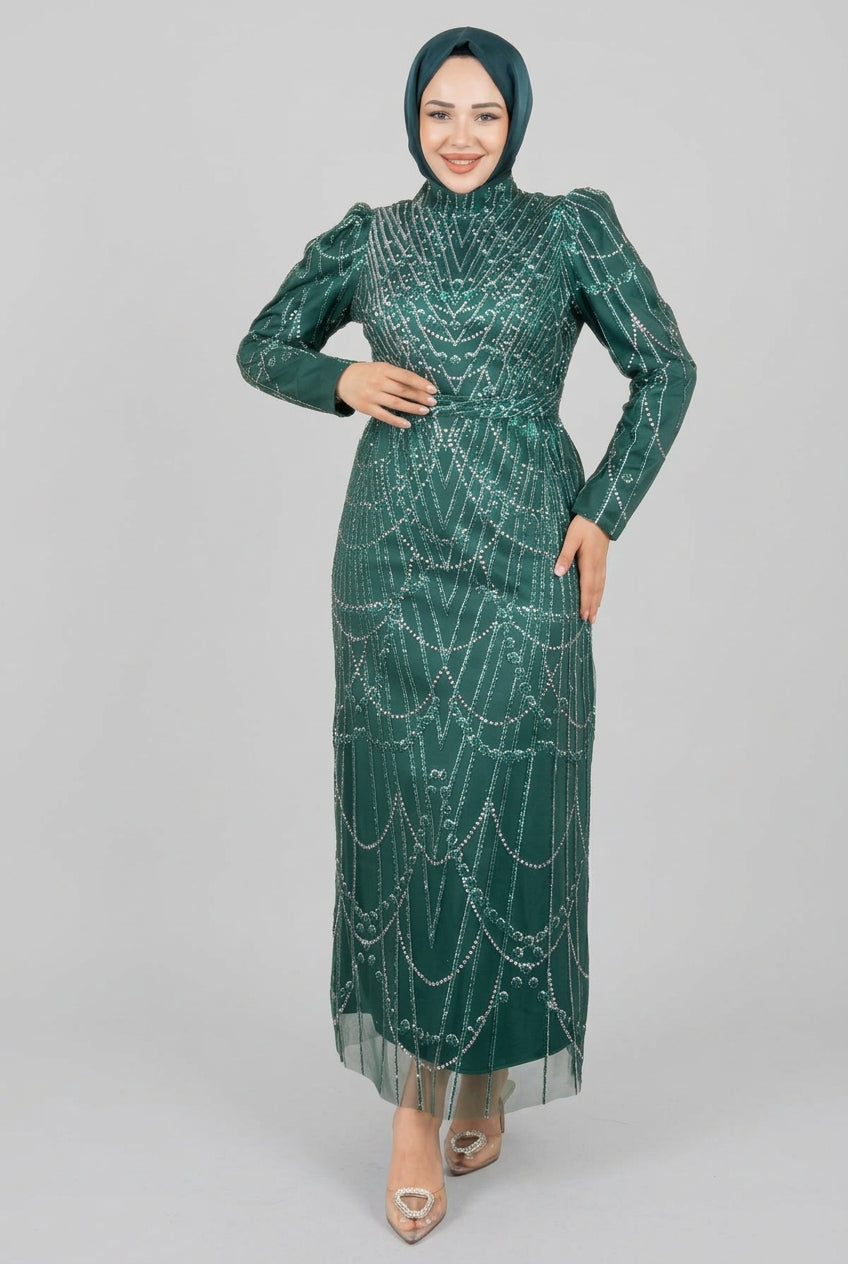 Woman in a green dress with a pattern standing indoors next to a plant.