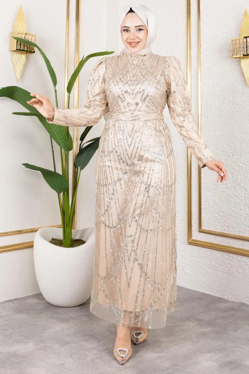 Woman in a beige dress standing next to a plant in an indoor setting