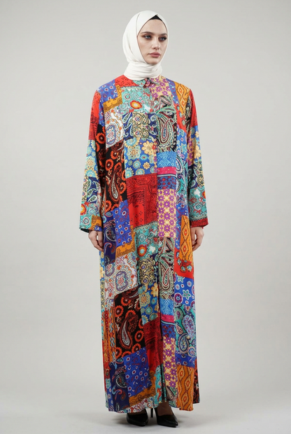 A woman wearing a white hijab and a long-sleeve button-up shirt with a highly colorful, busy patchwork paisley and floral print, posed against a solid slate blue background.