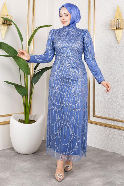Woman wearing a blue dress with intricate patterns in a room with a plant and framed picture.