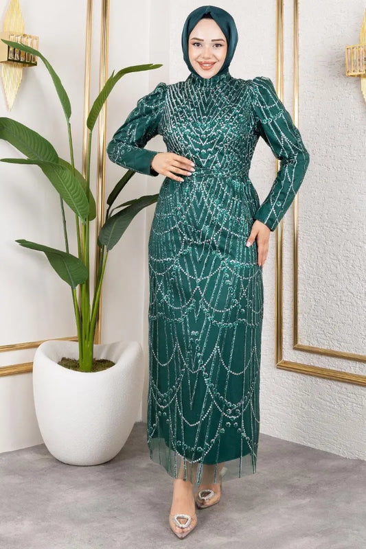 Woman in a green dress with a pattern standing indoors next to a plant.