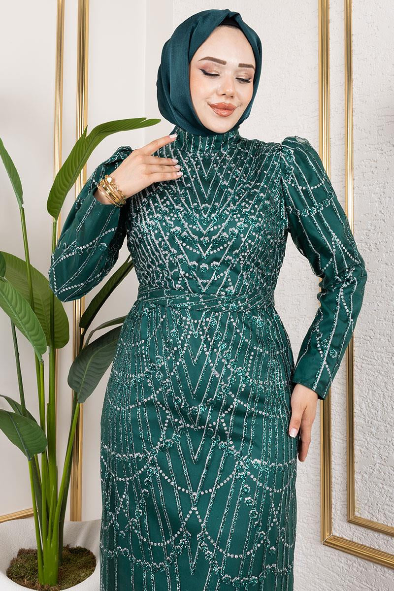 Woman wearing a green dress with intricate patterns in a room with a plant and framed pictures.
