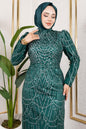 Woman wearing a green dress with intricate patterns in a room with a plant and framed pictures.