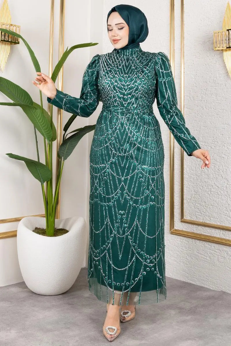 Woman wearing a green beaded dress standing next to a potted plant indoors.