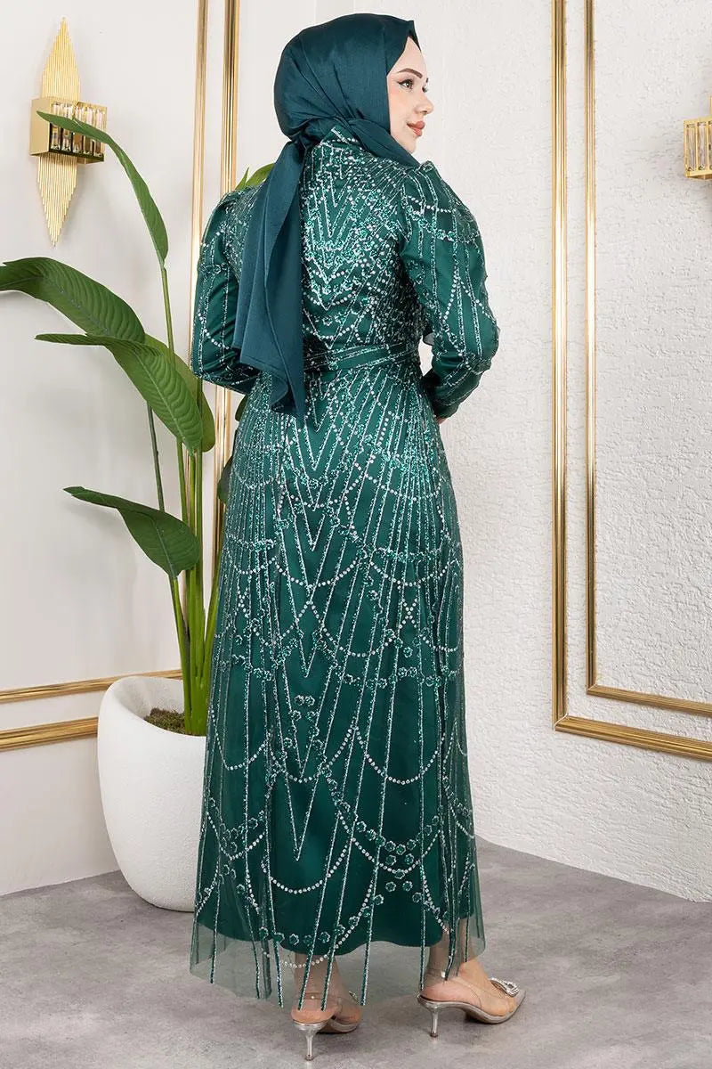 Woman wearing a green dress with intricate patterns and a matching hijab in an indoor setting.