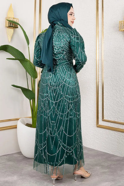 Woman wearing a green dress with intricate patterns and a matching hijab in an indoor setting.