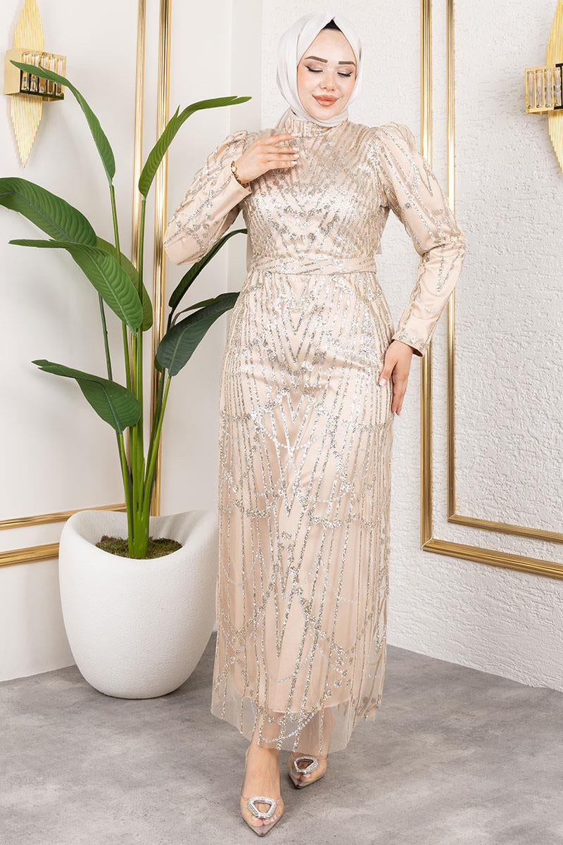 Woman in a sparkly dress standing in a room with a plant and decorative wall.