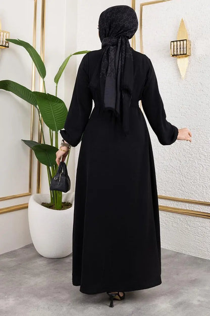 Person wearing a black abaya in a room with decorative elements.