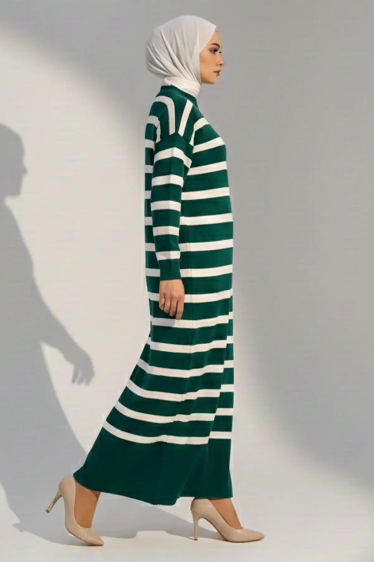 Woman wearing a green and white striped dress with a hijab against a plain background