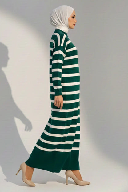 Woman wearing a green and white striped dress with a hijab against a plain background
