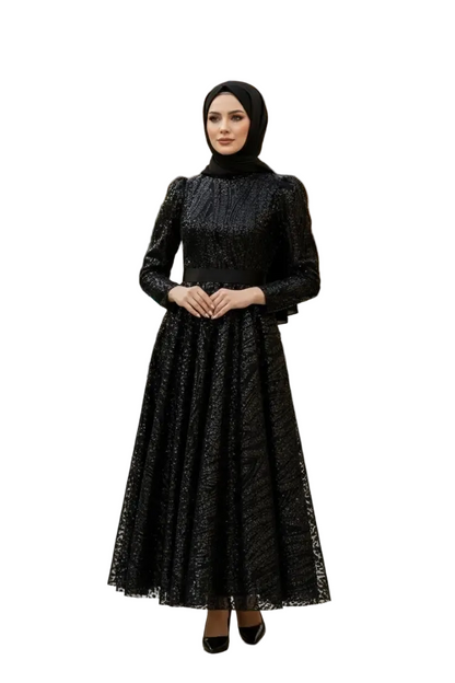 A woman wearing a long-sleeved black lace maxi dress with a matching black hijab, standing against a plain white background.